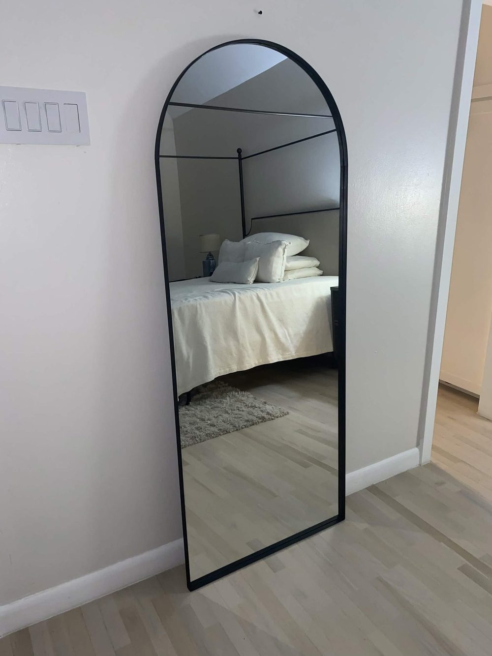 Black arched mirror leaning in a bedroom