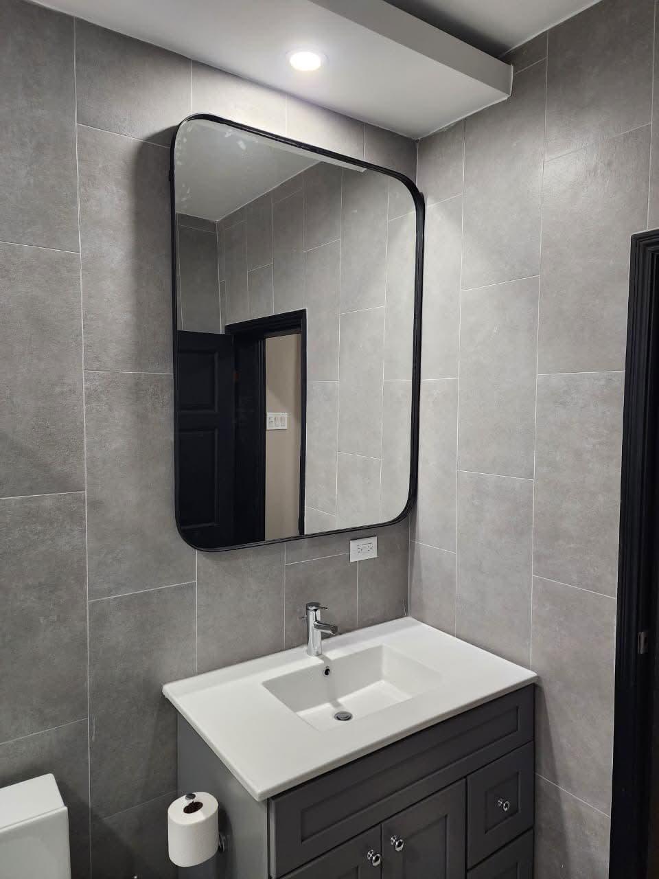 Rounded-corner rectangular mirror over a grey bathroom vanity